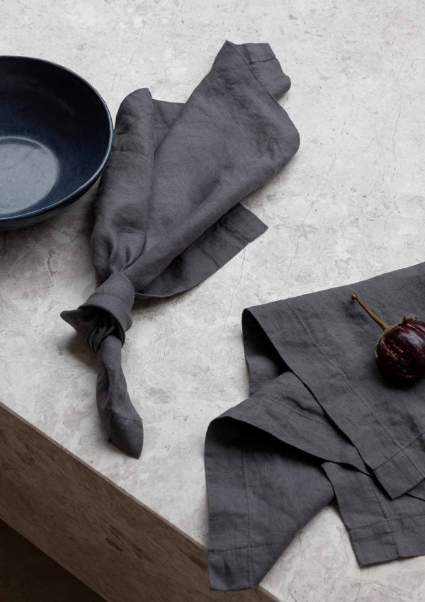 Graphite grey napkins with an eggplant and blue bowl on a stone surface.