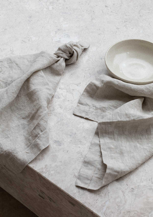 Natural coloured linen napkin on stone surface with a small ceramic bowl.