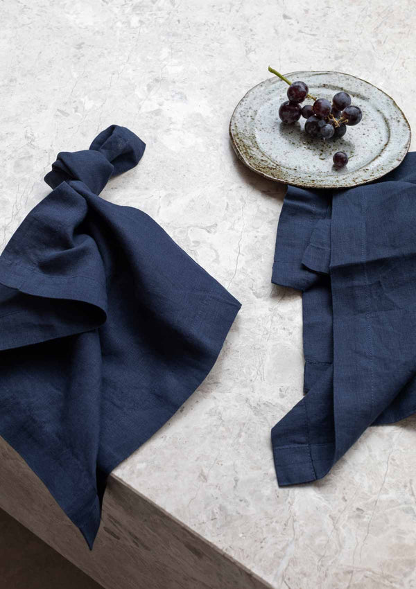 Linen navy napkin on a stone surface with a ceramic plate and purple grapes.