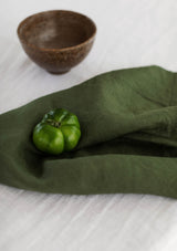Forest green linen napkin on a whote tablecloth with a green capsicum and wooden bowl.